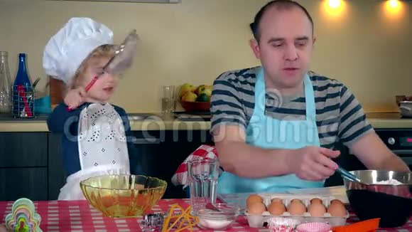 爸爸带着可爱的蹒跚学步的女孩在厨房准备蛋糕视频的预览图
