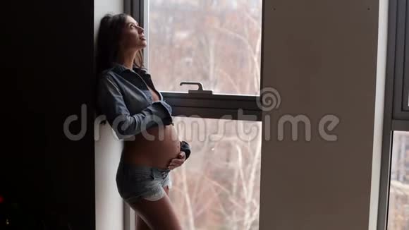 一个怀孕的女孩站在一扇大窗户附近视频的预览图