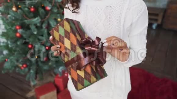 一个穿着毛衣和长袜的漂亮女孩坐在美丽的圣诞树旁手里拿着礼物视频的预览图
