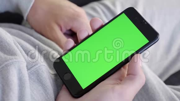 男人在家坐在沙发上拿着绿色的模拟屏幕智能手机视频的预览图