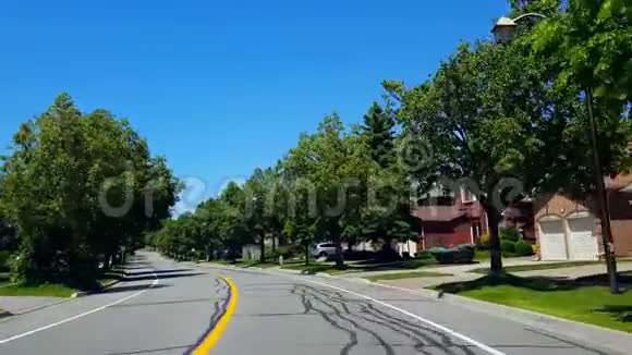 在夏日期间驾驶住宅城市道路上的树木沿着美丽的阳光郊区道路的司机视角视频的预览图