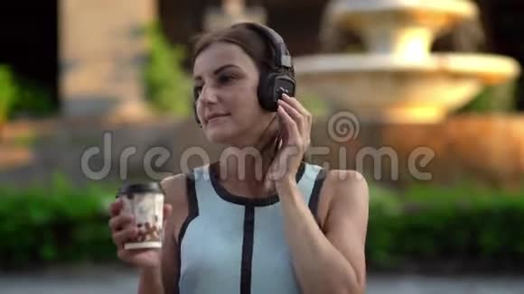 美丽的年轻女子使用智能手机打字听音乐在城市散步时喝咖啡视频的预览图