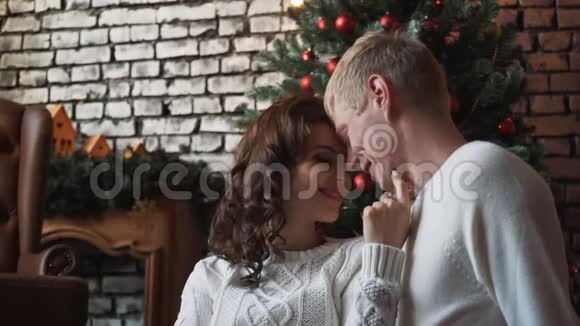 一个年轻英俊的丈夫拥抱他的妻子如果在新年树前礼物和橘子在他们周围家庭视频的预览图