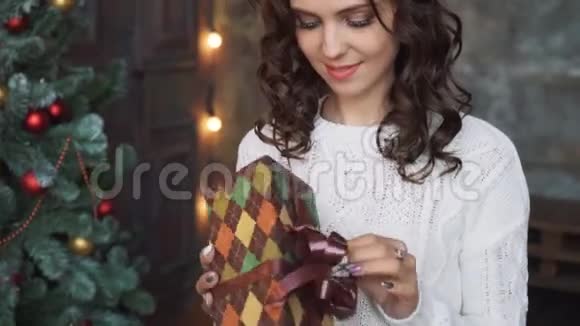 一个穿着毛衣和长袜的漂亮女孩坐在美丽的圣诞树旁手里拿着礼物视频的预览图