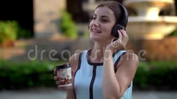 美丽的年轻女子使用智能手机打字听音乐在城市散步时喝咖啡视频的预览图