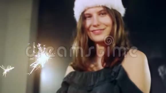一个女孩模特用手中的火花许愿的肖像圣诞帽圣诞女孩看着摄像机视频的预览图
