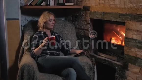 年轻女性使用数码平板电脑享受家中壁炉旁的冬季热饮视频的预览图