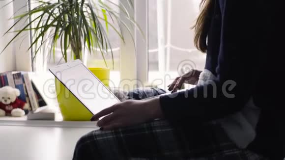 漂亮的年轻黑发女孩在靠近窗户的厨房里与平板电脑合作视频的预览图