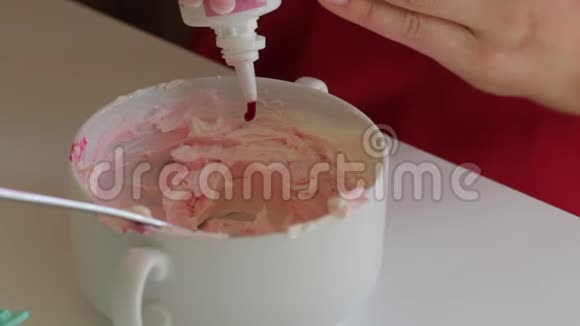 一个女人从一管奶油奶酪中加入一滴食用色素着色奶油以润滑蛋糕视频的预览图