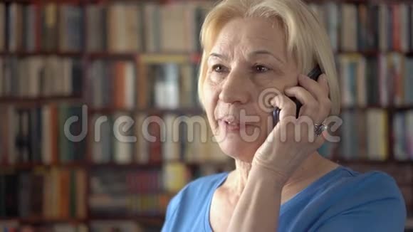 现代高级女性在家使用手机与朋友交谈背景书架视频的预览图