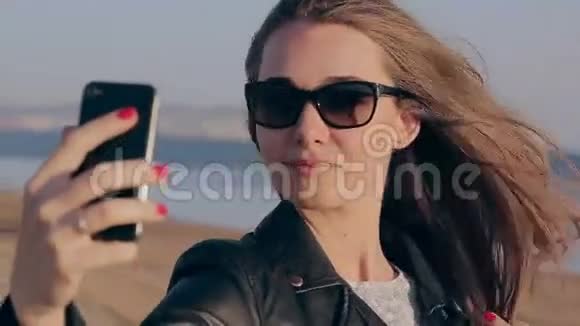 快乐的年轻女人在海滩上玩智能手机自拍照片时尚的女模特视频的预览图