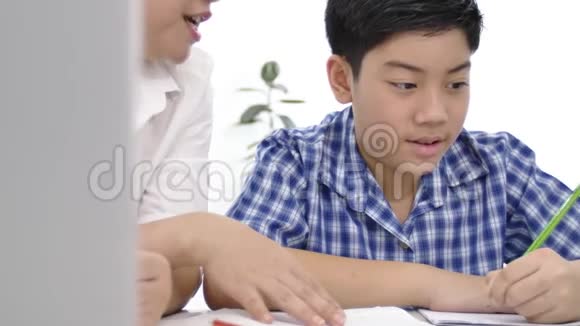 年轻的亚洲母亲在家教儿子亚洲妈妈带着儿子在桌子上做作业脸上带着微笑多利射了4K视频的预览图