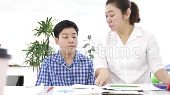 年轻的亚洲母亲在家教儿子亚洲妈妈带着儿子在桌子上做作业脸上带着微笑多利射了4K视频的预览图