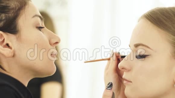 女人化妆师用化妆刷来化妆眼睛美容模特把脸贴紧做化妆脸视频的预览图