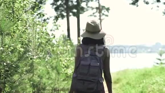 一位年轻漂亮的旅游女孩的肖像她背着背包戴着草帽沿着岩石海洋背景和视频的预览图