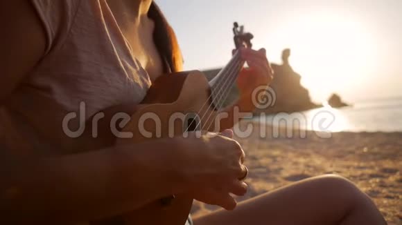 女孩坐在沙滩上弹着四弦琴吉他关闭高清慢镜头视频的预览图