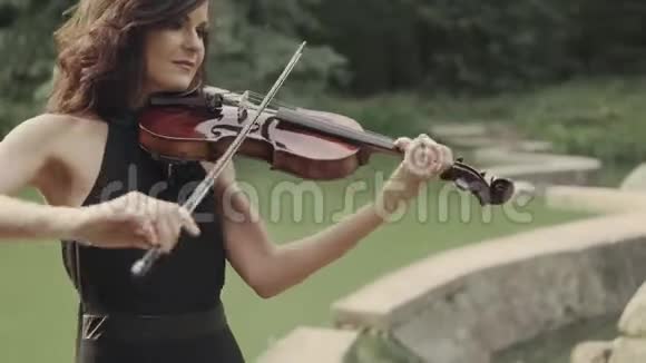 穿裙子的漂亮女孩在户外拉小提琴森林中优雅的小提琴手视频的预览图