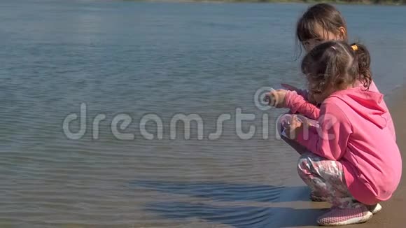 孩子们让船走带着纸船在河边的小女孩两个姐妹在水边玩视频的预览图
