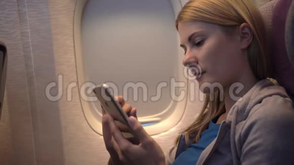 飞机窗户附近美丽迷人的女人长途飞行使用智能手机浏览视频的预览图