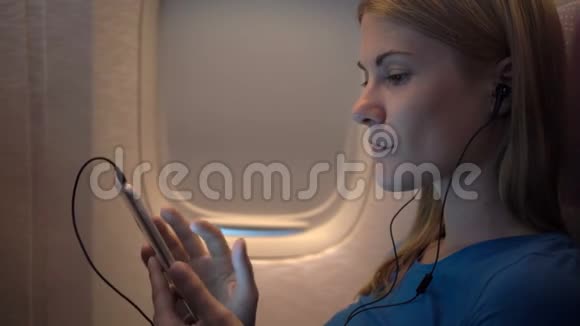 飞机窗户附近美丽迷人的女人长途飞行听智能手机上的音乐视频的预览图
