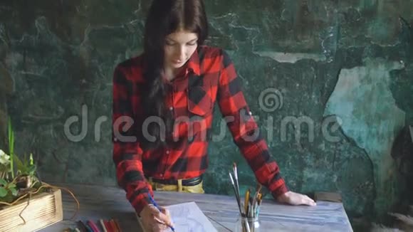 年轻的女艺术家在纸笔记本上画一幅画看着相机视频的预览图
