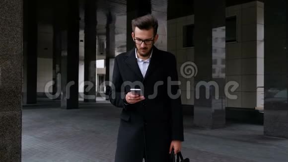 一位严肃的经理穿着经典的西装和眼镜手握智能手机键入一条短信看着摄像机视频的预览图