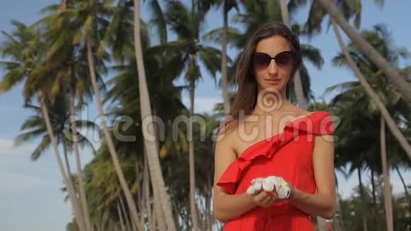 穿红色衣服的女孩靠近棕榈树她喜欢弗兰吉帕尼花视频的预览图