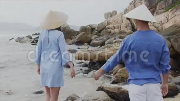 一个男孩和一个戴着越南帽子的女孩站在海边伸出双手紧紧地互相靠近概念视频的预览图