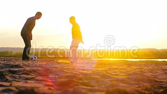 日落时分男人们在海滩上踢足球足球在阳光下在沙滩上滚动视频的预览图