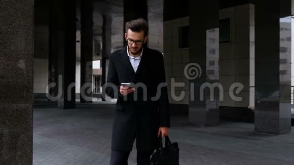一位严肃的经理穿着经典的西装和眼镜手握智能手机发短信看着摄像机视频的预览图