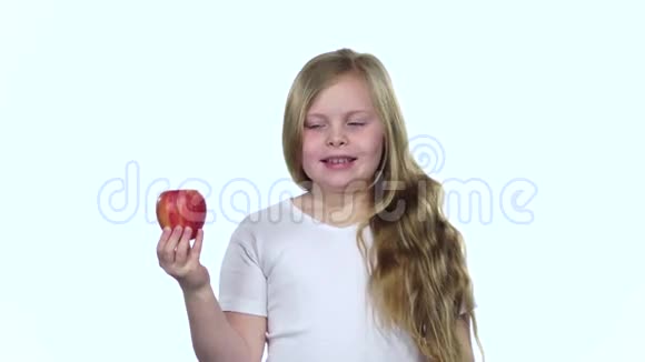 小女孩拿着一个苹果闻着它闻起来很香白色背景慢动作视频的预览图
