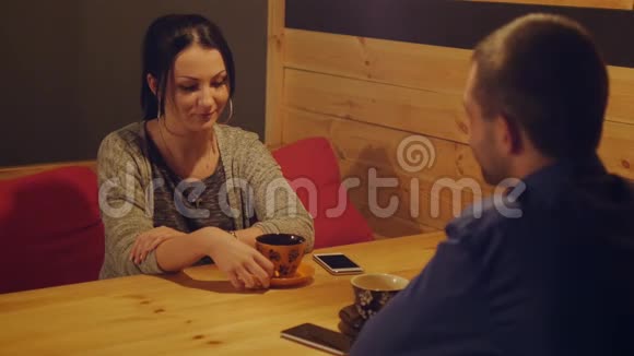 年轻夫妇坐在一张桌子旁的咖啡馆里喝着咖啡聊天女孩脸上带着微笑两个情人享受夜晚视频的预览图