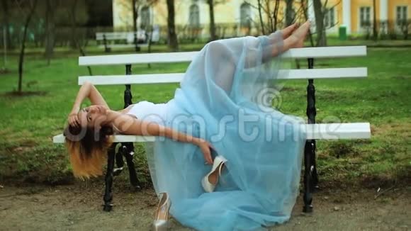 穿着白色和蓝色连衣裙的漂亮女孩躺在长凳上光着脚移动在拍照时处理高脚鞋视频的预览图