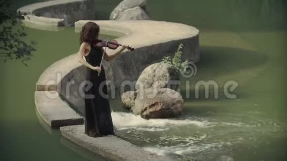 穿着黑色连衣裙拉小提琴呆在桥上户外的年轻漂亮女孩视频的预览图