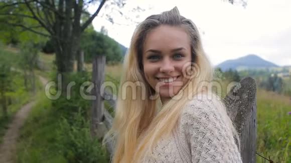 美丽的女孩看着相机在森林和山村的背景上微笑视频的预览图