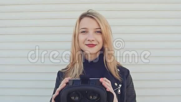 一个年轻时尚的金发女郎穿着皮夹克靠近水平滚筒百叶窗给相机带来虚拟眼镜视频的预览图