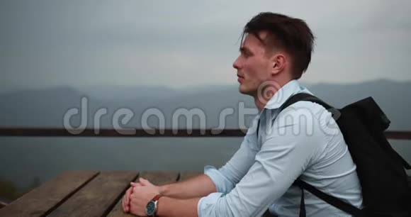 孤独的人在山里年轻的帅哥把头靠在手臂上坐在桌子旁视野很好视频的预览图