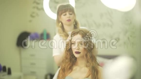 专业理发师发型师沙龙在金发波浪型女模特头上固定珍珠皇冠珠宝首饰上的饰物视频的预览图
