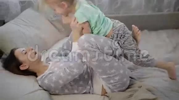 妈妈和女儿在卧室里带着孩子的女孩躺在床上玩耍穿着t恤的婴儿视频的预览图