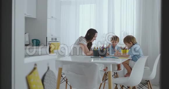 两个男孩的孩子和他的母亲坐在厨房里画画视频的预览图