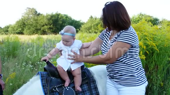 一个带着孩子的女人在田野里走来走去一个婴儿坐在小马上妈妈抱着孩子快乐的家庭假期视频的预览图