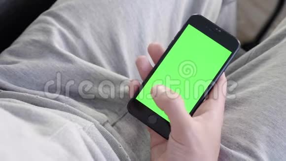 男人在家坐在沙发上使用带有绿色模拟屏幕的智能手机视频的预览图