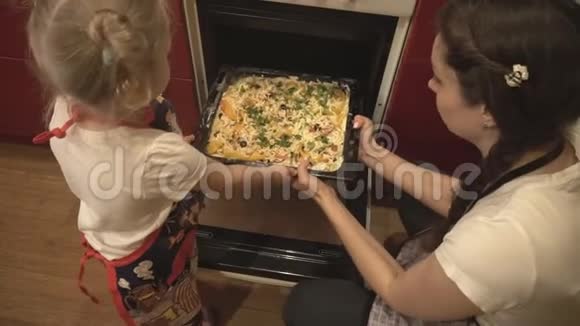 一位母亲和她的女儿把锅和披萨一起放进烤箱视频的预览图