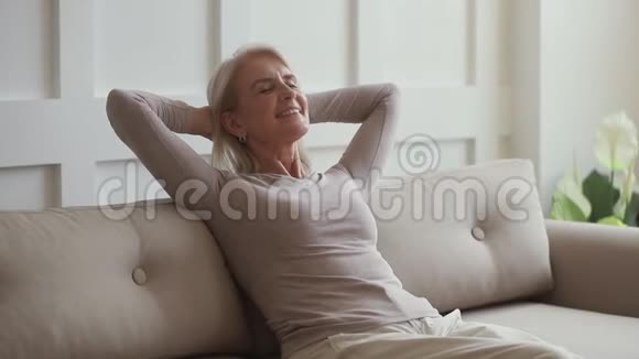 快乐的中年妇女坐在家里的沙发上放松视频的预览图