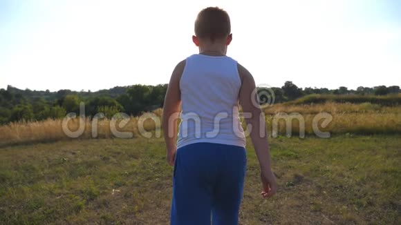 在阳光明媚的日子里小男孩在草地上奔跑儿童在户外草坪慢跑快乐视频的预览图