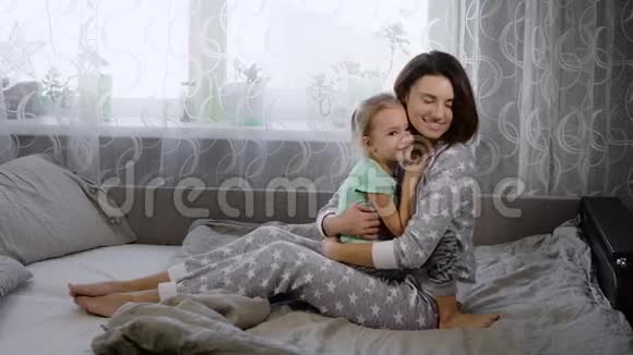 年轻的母亲穿着睡衣女儿在卧室的床上玩得很开心在的陪伴下彼此享受着视频的预览图