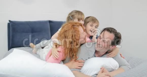 幸福的微笑家庭在卧室孩子和父母沟通在一起躺在父亲床上早上视频的预览图