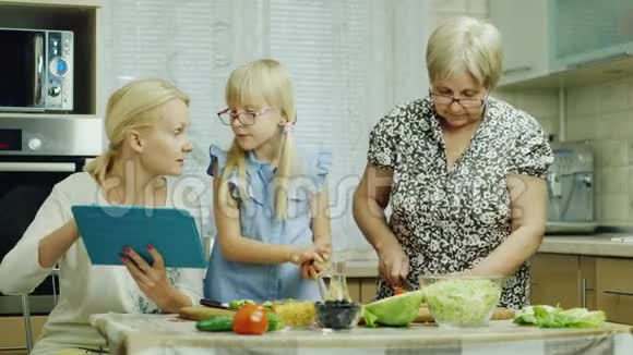 祖母母亲和孙女在厨房里一起做沙拉好好享受平板电脑玩得开心视频的预览图