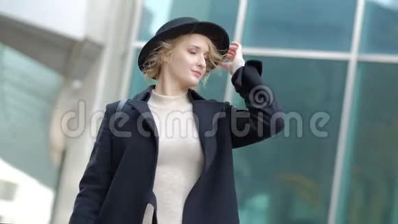 女子玩现代黑色帽子移动宽边黑大衣底部在街上慢动作低角度拍摄视频的预览图