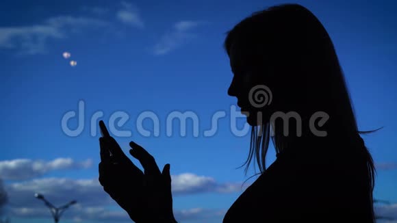 使用电话的女性剪影黑色轮廓女性使用智能手机背景的蓝天视频的预览图
